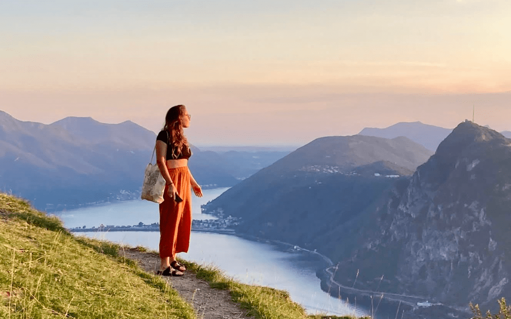 Person standing on a hill, watching the sunset over Lake Lugano.